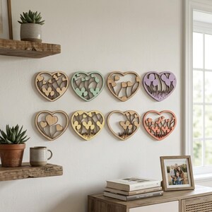May include: Eight wooden heart-shaped wall decorations with floral designs in various pastel colors. The hearts are mounted on a white wall, creating a decorative display. The hearts are made of wood and have a natural wood grain.