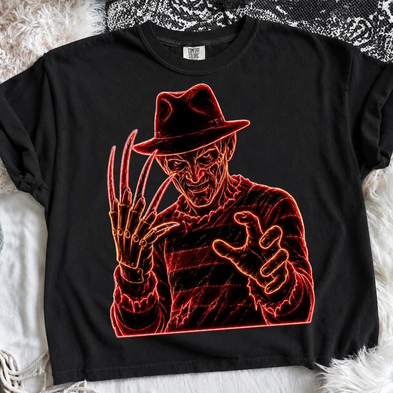 May include: A black t-shirt featuring a neon red graphic illustration of a character wearing a fedora hat and a striped sweater, with a clawed glove on one hand. The design has a glowing outline effect against the dark fabric of the shirt.