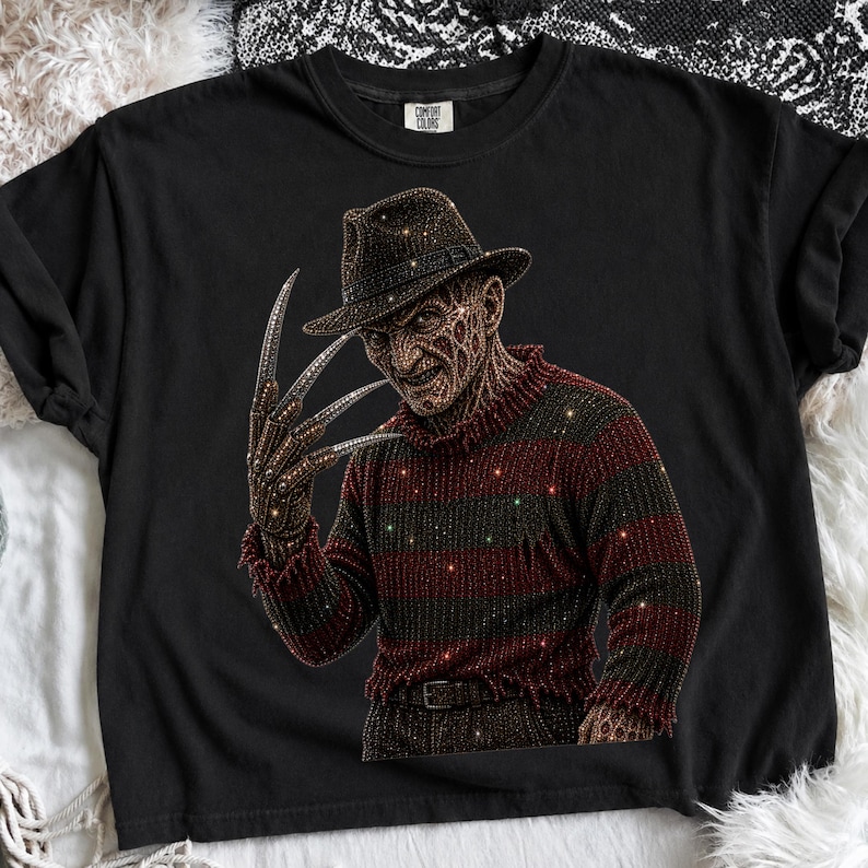 May include: A black short-sleeve t-shirt featuring a graphic print of a character wearing a brown fedora and a red and dark brown striped sweater. The character has a scarred face and a glove with long, sharp metal blades on the fingers.