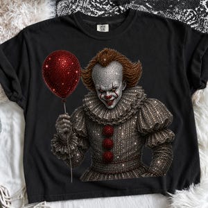May include: A black short-sleeved t-shirt featuring a graphic of a clown with a white face, red makeup, and a ruffled collar. The clown is holding a red balloon. The entire graphic is rendered in a sparkling, rhinestone-like texture.