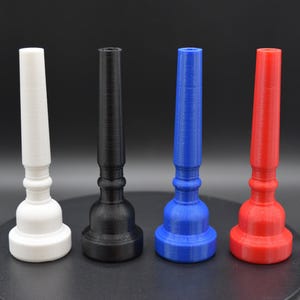 May include: Four colorful 3D-printed objects in white, black, blue, and red. Each has a flared base, a central bulbous section, and a long, cylindrical top. The objects are arranged in a row against a dark background.