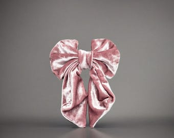 Peut inclure: Un grand nœud en velours rose poudré. Le nœud est centré et a une forme classique avec deux boucles et de longues queues fluides. Le tissu a un éclat doux et lustré.