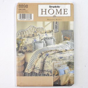 May include: A Simplicity Home Bedding Basics sewing pattern envelope 8898. The front features illustrations of a bed with floral and plaid patterned bedding, including ruffled pillows and a bed skirt, plus a smaller inset image of blue bedding.