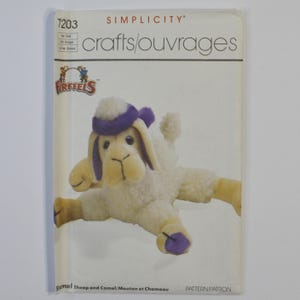 May include: A Simplicity 7203 sewing pattern envelope for Firefels crafts featuring a plush sheep with cream-colored fur, purple ear accents, and purple hooves. The text on the cover includes Simplicity, 7203, crafts/ouvrages, Firefels, and Sheep and Camel.