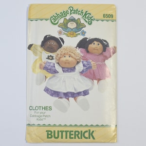May include: A vintage Butterick pattern for Cabbage Patch Kids clothes. The cover features illustrations of three Cabbage Patch Kids dolls wearing different outfits. The pattern number is 6509. The text "CLOTHES For your Cabbage Patch Kids!" is also visible.