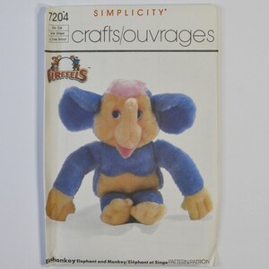 May include: A Simplicity 7204 crafts pattern envelope featuring a Firffels character, an elephant-monkey hybrid plush toy with blue fur, a tan face, and a pink tuft of hair. The text reads Simplicity 7204, crafts/ouvrages, Firffels, and Elephant and Monkey.