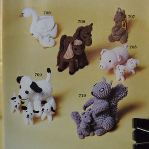 May include: A collection of crocheted animal figures including a white swan 706, a brown horse 708, a grey squirrel 707, a pink pig with piglets 705, a black and white dog with puppies 709, and a grey squirrel with a baby squirrel 710.