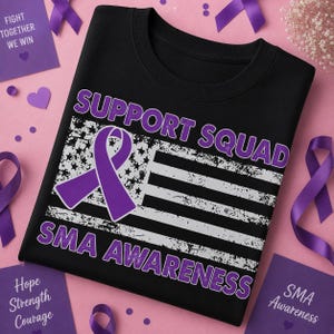 May include: A black t-shirt featuring a distressed white American flag graphic with a purple awareness ribbon overlay. The text reads SUPPORT SQUAD in purple above the flag and SMA AWARENESS in purple below the flag, all in a bold sans-serif font.