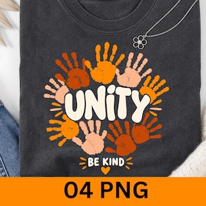 May include: A charcoal grey t-shirt featuring a circular arrangement of handprints in various shades of orange, brown, and cream. The centre text reads "UNITY" in large white letters, with "BE KIND" and a small heart icon below it.