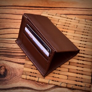 Puede incluir: Una cartera de cuero marr&oacute;n con dos tarjetas visibles en un bolsillo delantero. La cartera est&aacute; abierta, revelando el interior. La cartera est&aacute; sobre una superficie de madera.