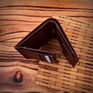 Puede incluir: Cartera de cuero marr&oacute;n abierta con m&uacute;ltiples ranuras para tarjetas y un compartimento para billetes. La cartera se muestra abierta, revelando su interior. El fondo es una superficie de madera y una esterilla de bamb&uacute;.