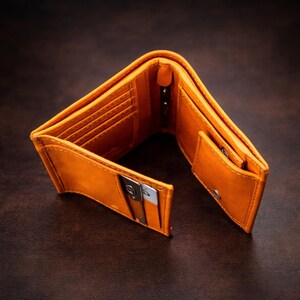 Puede incluir: Cartera de cuero naranja abierta con m&uacute;ltiples ranuras para tarjetas, un compartimento para billetes y un peque&ntilde;o bolsillo para monedas. La cartera est&aacute; hecha de cuero liso y tiene un dise&ntilde;o cl&aacute;sico. La cartera est&aacute; abierta, mostrando su interior.
