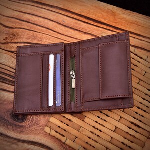 Puede incluir: Cartera de cuero marr&oacute;n abierta con m&uacute;ltiples ranuras para tarjetas, un compartimento con cremallera y un billetero. La cartera est&aacute; hecha de cuero cosido y se muestra abierta, mostrando su dise&ntilde;o interior. El fondo es una superficie de madera.