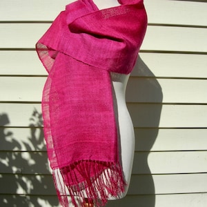 May include: A bright pink silk scarf with fringe on the ends. The scarf is draped over a white mannequin.