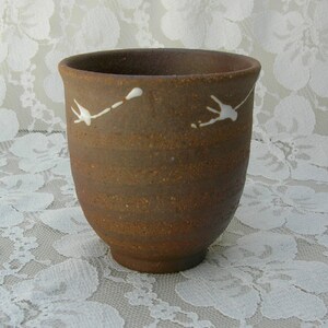 May include: A brown ceramic teacup with white bird designs. The cup has a rounded shape and a slightly flared rim.