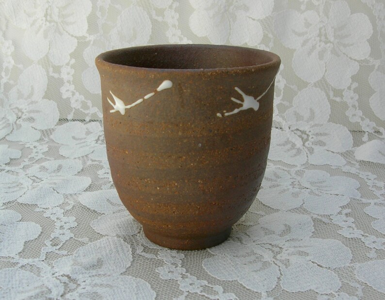 May include: A brown ceramic teacup with white bird designs. The cup has a rounded shape and a slightly flared rim.