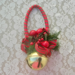 May include: A gold bell with a red and green ribbon and red berries. The bell is attached to a red and white striped handle.