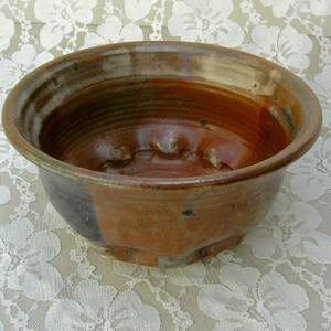 May include: A brown ceramic bowl with a textured, uneven surface and a white rim. The bowl has a dark brown glaze on the outside and a lighter brown glaze on the inside.