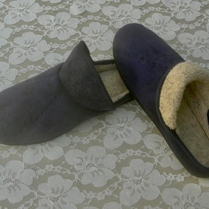 May include: A pair of dark blue suede slippers with a soft, light brown fleece lining. The slippers have a closed toe and a slip-on design.