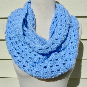 May include: A light blue crocheted infinity scarf. The scarf is made with a delicate open stitch pattern.