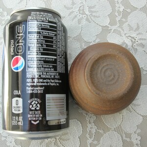 May include: A black can of Pepsi One cola with the nutrition facts listed on the side. The can is next to a small, brown ceramic bowl.