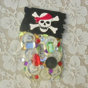 May include: A light switch cover decorated with a pirate skull and crossbones, surrounded by gold coins and colorful jewels.