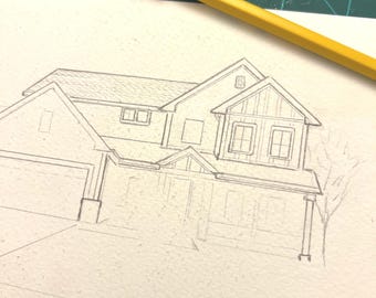 May include: A graphite pencil sketch on white paper depicting a two-story house with a garage, multiple gabled roof sections, and windows. A yellow pencil with an orange eraser is positioned diagonally across the top of the drawing.