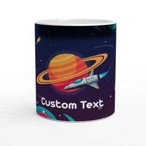 May include: White ceramic mug featuring a space-themed design. The design includes a planet with rings, a rocket ship, and the words "Custom Text" in white. The background is a dark blue with stars and other planets.