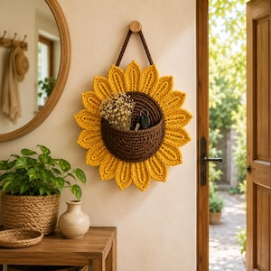 May include: A sunflower-shaped wall hanging made of crocheted yarn with bright yellow petals and a dark brown center pocket. The pocket contains a small bunch of dried white flowers and a set of black keys, suspended by a brown yarn loop.
