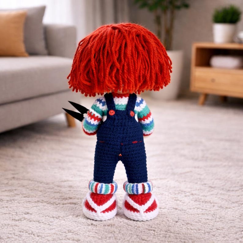 May include: A handmade crochet doll with red yarn hair, wearing a striped sweater, blue overalls, and red and white shoes. The doll is holding black scissors. The doll is standing on a carpeted floor.