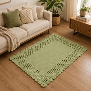 Puede incluir: Una alfombra rectangular de color verde salvia con un panel central sólido rodeado por un borde ancho de ganchillo intrincado con un patrón de rejilla y un borde festoneado. La alfombra está hecha con un acabado de hilo texturizado.