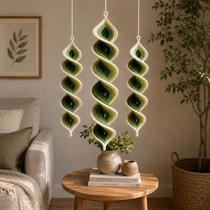May include: Three hanging spiral decorations crafted from yarn in an ombre gradient of cream, light green, and dark forest green. Each piece features a twisted, elongated shape suspended by a thin white string, showcasing a textured crochet stitch.