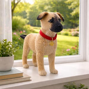 May include: A crocheted dog figurine in tan, black, and red. The dog has a red collar with a gold tag. The dog is standing on a white windowsill with a green background.