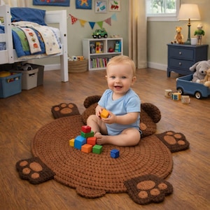 May include: A brown, round, crocheted rug shaped like a bear with paw details. A baby in a blue onesie sits on the rug, playing with colorful wooden blocks. The rug is on a wooden floor.