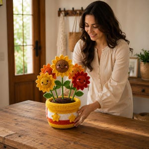 May include: A crochet potted plant featuring five sunflowers with smiling faces in yellow, orange, and red. The flowers have green stems and leaves, and they are planted in a yellow, white, and orange striped crochet pot decorated with two yellow stars.