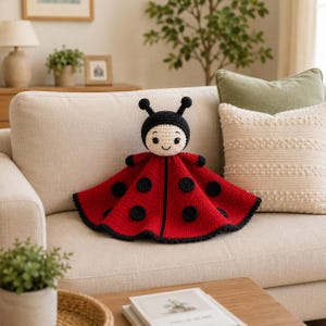 May include: A handmade crochet ladybug toy featuring a round cream-colored face with black embroidered eyes and a smile, topped with two black antennae. The body is a wide, red, circular crocheted piece adorned with several black circular spots.