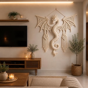 May include: A large, cream-colored macrame dragon wall hanging with outstretched wings, intricate knotwork, and a detailed head. The dragon is the focal point of a neutral-toned living room with wooden furniture and decorative plants.