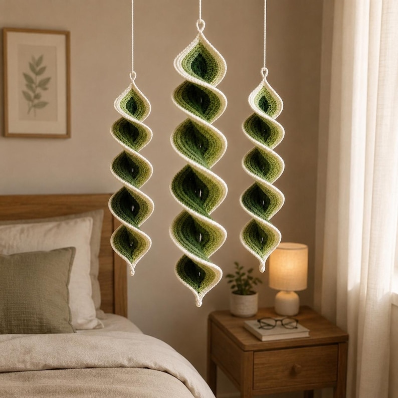 May include: Three hanging spiral ornaments crafted from yarn in an ombre gradient of cream, light green, and dark forest green. Each piece features a continuous twisted shape suspended by a thin white string, creating a vertical decorative display.