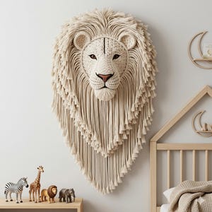 May include: A large, off-white lion head wall hanging. The lion's face is intricately crocheted with detailed features, including brown eyes and a tan nose. The mane is made of long, flowing strands, creating a textured, decorative piece. The wall hanging is mounted on a white wall.