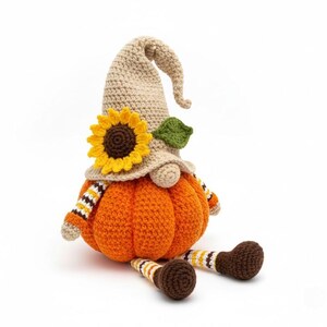 May include: A handmade crochet gnome with an orange pumpkin body, beige hat, and brown legs. The hat is adorned with a sunflower and green leaf. The arms have orange and white striped sleeves. A whimsical fall decoration.