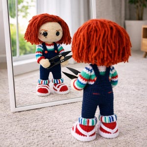May include: Crocheted doll with orange hair, blue overalls, and striped shirt and socks, holding black scissors. The doll is reflected in a mirror. The doll's red and white sneakers complete the look.