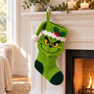 Pode incluir: Uma meia de Natal em crochê verde-limão com o rosto de um personagem de olhos amarelos, um sorriso largo e um punho branco decorado com bagas de azevinho vermelhas e folhas verdes. A meia tem a ponta e o calcanhar em verde escuro.