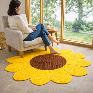 Puede incluir: Una alfombra grande de girasol hecha a mano con un centro marrón y pétalos amarillos. La alfombra está hecha de hilo grueso y texturizado y se coloca sobre un piso embaldosado. Es un artículo decorativo para una sala de estar o dormitorio.
