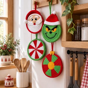 May include: Four round, crocheted ornaments hanging from a wooden rack. One features a Santa Claus face, one a green character with a red hat, one a red and white peppermint swirl, and one a red, green, and yellow geometric pattern design.