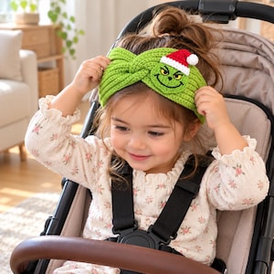 Op de afbeelding: Een limoengroene gehaakte hoofdband met een gedraaid knoopontwerp in het midden. De hoofdband is versierd met een klein, geborduurd groen karaktergezicht met een rood-witte kerstmuts met een witte pompon op de bovenhoek.