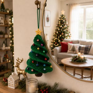 May include: A green crocheted Christmas tree ornament hanging from a hook. The tree features a spiral design with a yellow crocheted star at the top, a brown base, and small, colorful spherical beads attached throughout the green yarn layers.