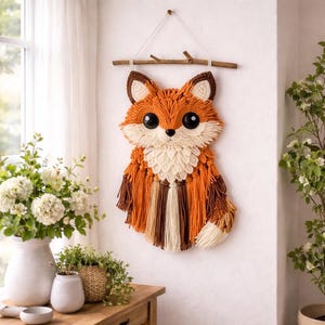 Peut inclure: Décoration murale en forme de renard, réalisée en fil orange, marron et crème. Le renard a de grands yeux noirs et est suspendu à une branche de bois par une ficelle blanche. Une décoration charmante pour une chambre d'enfant.