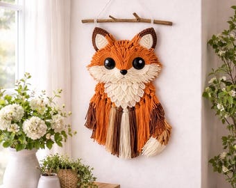 May include: A decorative fox wall hanging, crafted from orange, brown, and cream yarn. The fox features large black eyes and is suspended from a wooden branch with a white string. This handmade piece is a charming addition to a child's room or nursery.