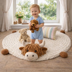 May include: A smiling toddler in a blue onesie holds a brown stuffed dog. A beige teddy bear sits on a white, round, knitted rug. A crocheted Highland cow head and several brown crocheted balls are also on the rug.