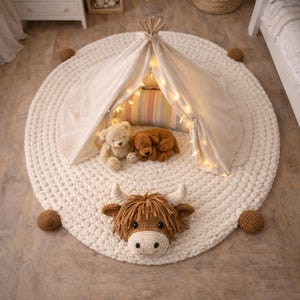 May include: A cream-colored, round, crocheted play mat with a small teepee, fairy lights, and stuffed animals. A brown Highland cow head is attached to the mat. Decorative brown balls are placed around the mat.